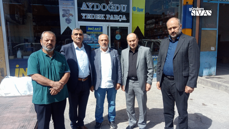 Üzerinde “AYDOĞDU YEDEK PARÇA” yazan iş yeri önünde beş erkek yan yana duruyor.