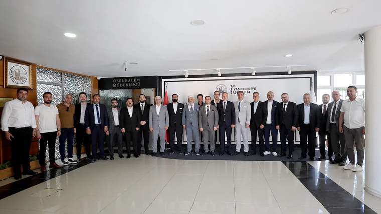 Sivas Belediyesi binasında, resmi kıyafetler giymiş bir grup insan, poz veriyor.