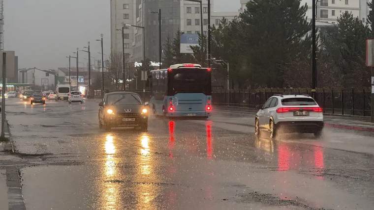 Yağmur nedeniyle su birikintileri oluşmuş caddede araçlar ilerliyor.