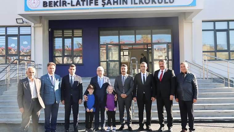 Bekir-Latife Şahin İlkokulu girişinde, okul tabelasının önünde duran sekiz yetişkin ve iki çocuk