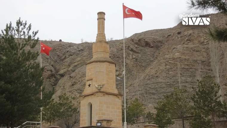 Yüksek bir taş yapıda Türk bayrağı ve başka bir bayrak dalgalanıyor, arka planda kayalık bir alan var.
