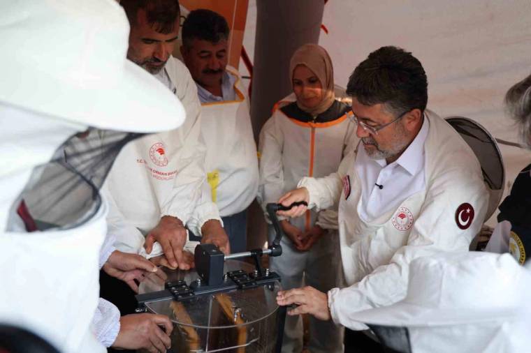 Beyaz önlüklü ve başlıklı kişiler, metal bir cihazın başında çalışırken görülüyor.