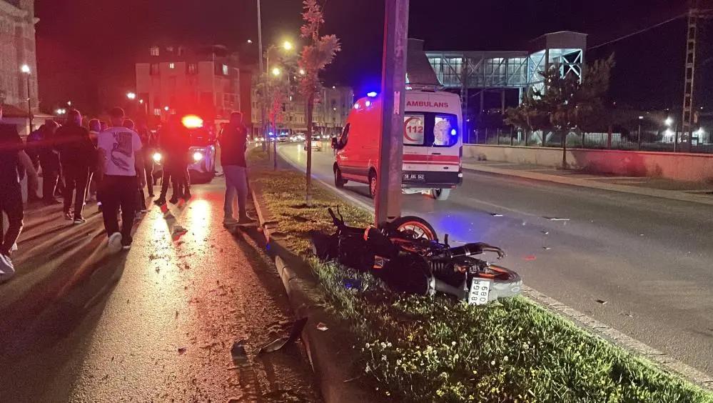 Yerde devrilmiş bir motosiklet, çevresinde ambulans ve kalabalık insanlar var.