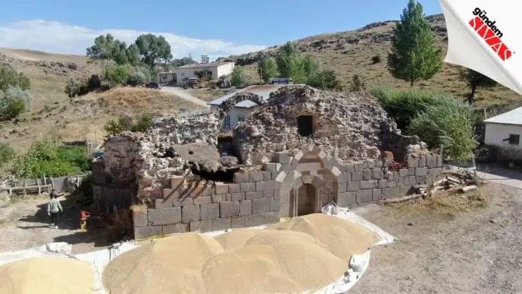 Yıkık bir tarihi yapı, önünde kum yığınlarıyla birlikte görünmekte.