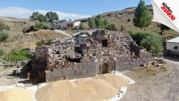Yıkık bir tarihi yapı, önünde kum yığınlarıyla birlikte görünmekte.