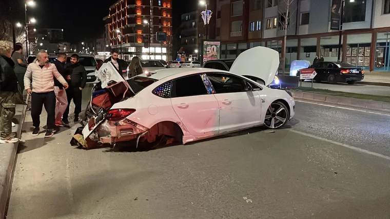 Yolda devrilmiş beyaz bir otomobil, çevresinde toplanmış insanlar var.