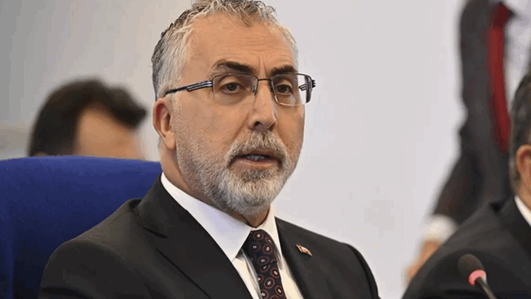 Kırmızı kravat takan, gözlüklü bir kişi, mavi bir sandalyede oturuyor.