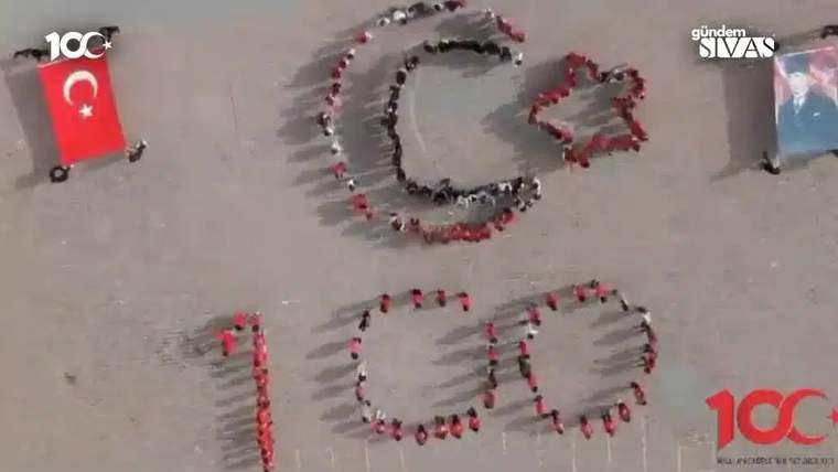 Kırmızı tişörtlü öğrenciler, yerde Türk bayrağı ve '100' yazısı oluşturmuş.