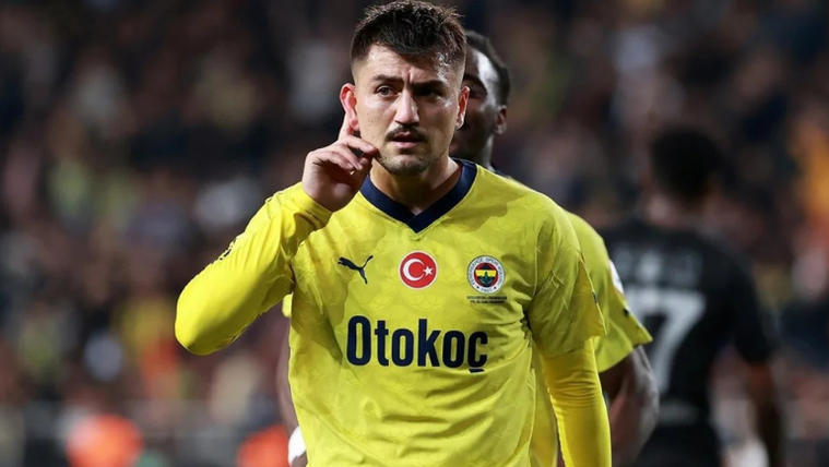 Fenerbahçe forması giymiş bir futbolcu, elini başının yanına getirerek dinleme pozisyonunda duruyor.