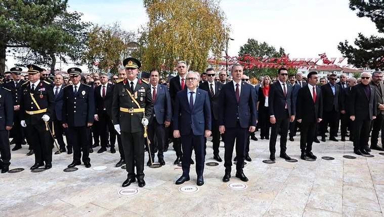 Üniformalı görevliler ve takım elbiseli kişiler, açık alanda yan yana yürürken görülüyor.