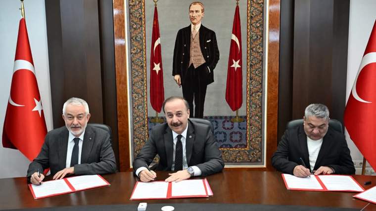 Üç kişi, masada belgeleri imzalıyor; arka planda Atatürk portresi ve Türk bayrakları var.