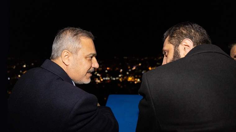 İki kişi, karanlık bir ortamda yan yana oturmuş, sohbet ediyor.
