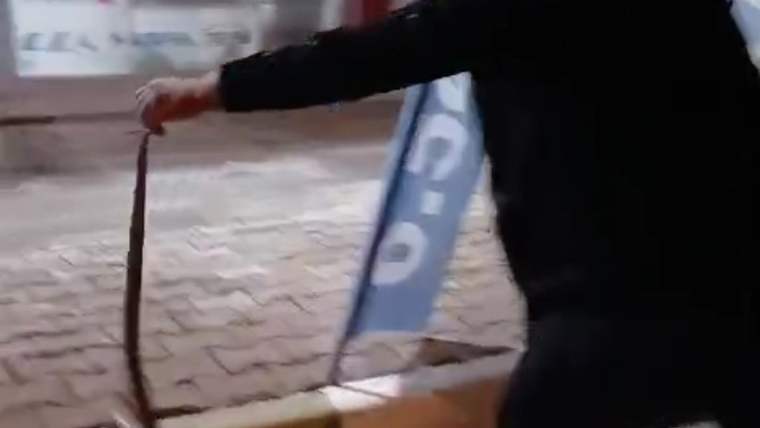 Siyah giyimli bir kişi, kaldırım önünde uzun ve ince bir yılanı elinde tutuyor.