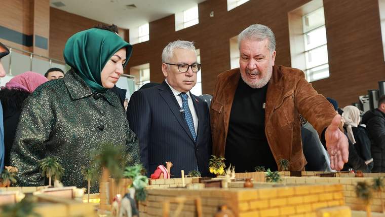 Bir kadın ve iki erkek, sergideki bir modelin önünde durarak konuşuyorlar.