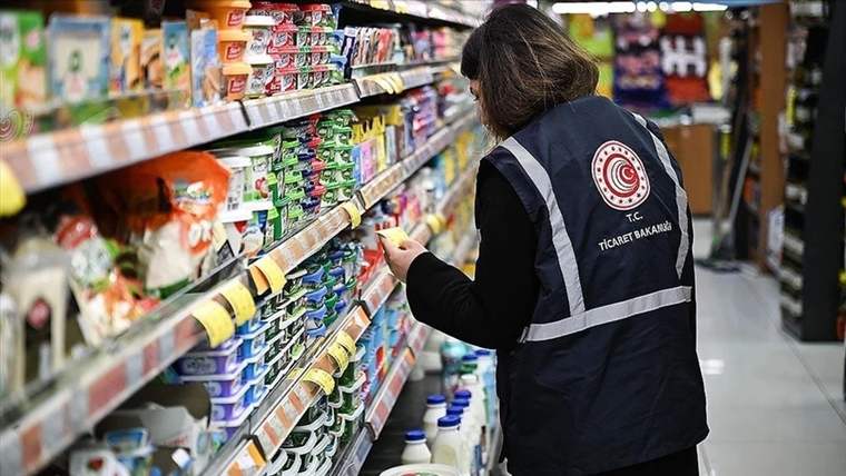 Market rafındaki ürünleri inceleyen, üzerinde T.C. Ticaret Bakanlığı yazılı yelek bulunan kişi