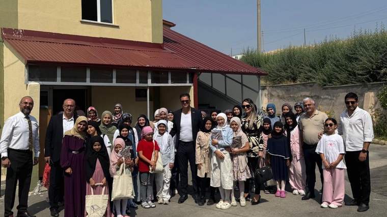 Kız öğrenciler ve MÜSİAD üyeleri, bir binanın önünde topluca poz veriyor.