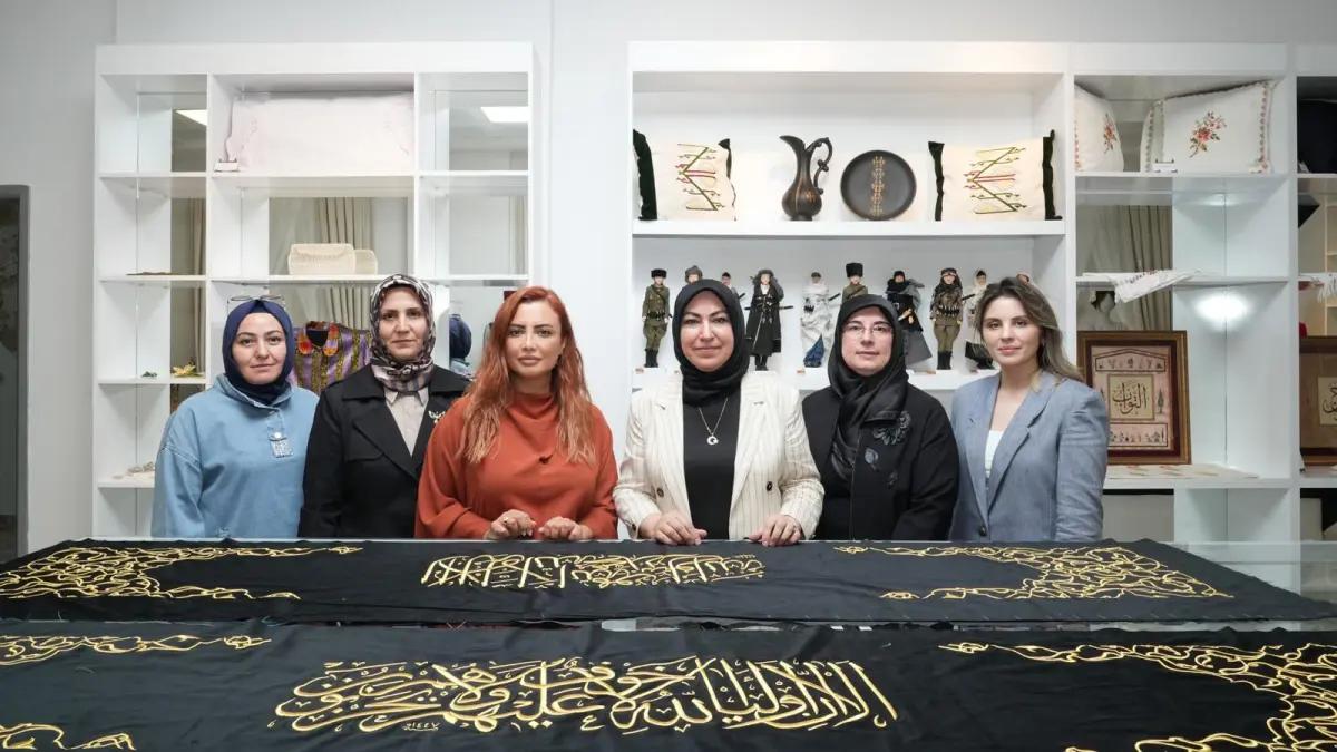 Altı kadın, siyah bir örtünün önünde duruyor; örtü üzerinde altın renkli yazılar var.