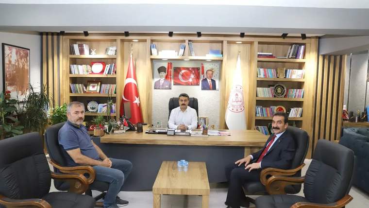 Bir masanın etrafında oturan üç kişi, arka planda Türk bayrağı ve Sivas'ın simgeleri var.