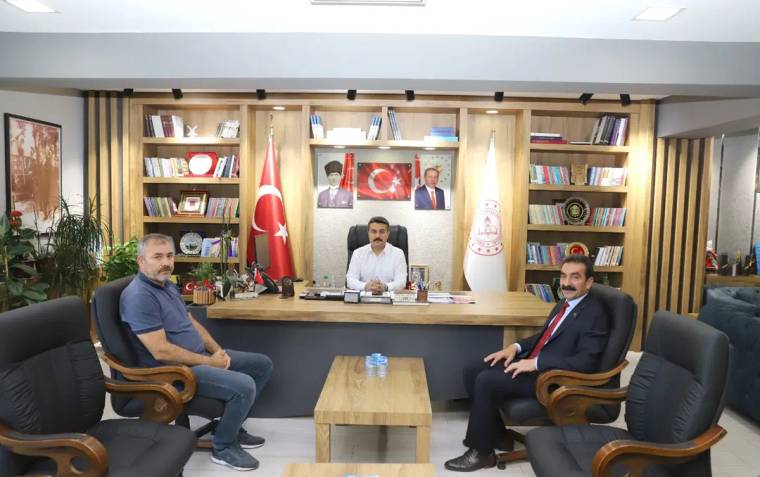 Bir masanın etrafında oturan üç kişi, arka planda Türk bayrağı ve Sivas'ın simgeleri var.