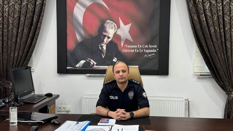 Makam odasında üniformalı bir kişi masada oturuyor; arkasında Türk bayrağı ve Atatürk portresi bulunuyor.