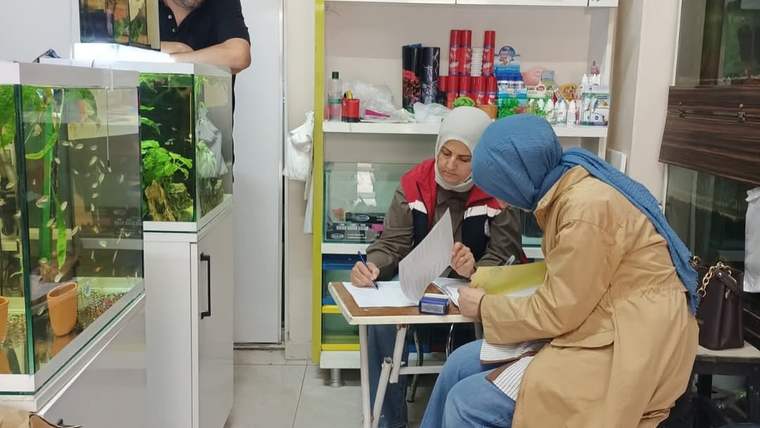 Evcil hayvan ürünlerinin bulunduğu dükkânda iki kadın evrak doldururken, akvaryumlar ve bir erkek görülüyor.
