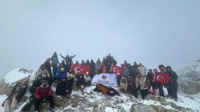 Karla kaplı dağ zirvesinde, Türk bayrağı ve yazılı pankartla grup fotoğrafı çekilmiş.