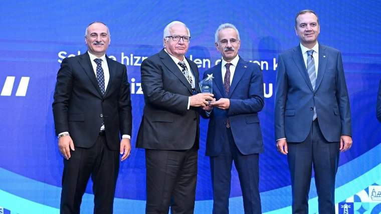 Mavi sahne fonu önünde dört takım elbiseli erkekten ikisi, küçük bir ödül heykelciği tutuyor.