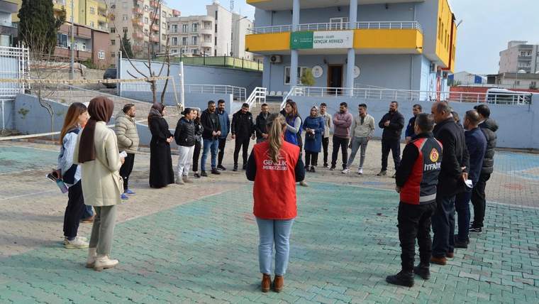 Gençlik merkezi binası önünde, kırmızı yelekli bir kişinin çevresinde toplanan bir grup görülüyor.