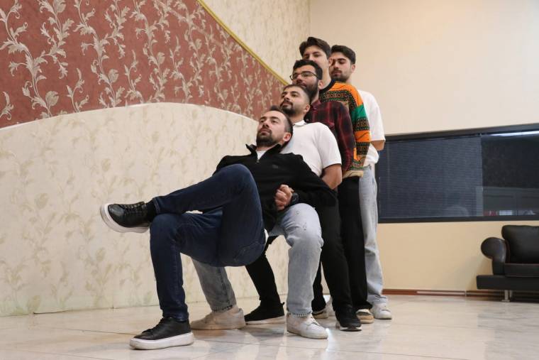 Bir salonda beş kişi, birbirlerinin arkasında sıralanarak bacaklarını öne uzatıp duruyor.