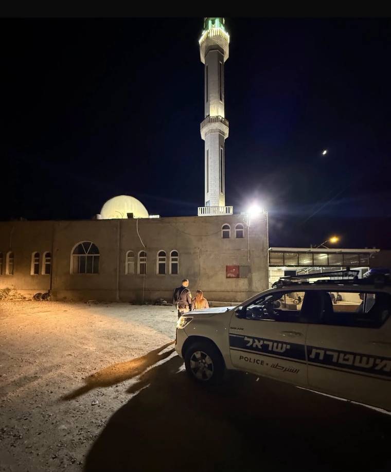 Gece aydınlatılan cami önünde, üzerinde polis yazıları bulunan bir araç ve iki kişi görülüyor.