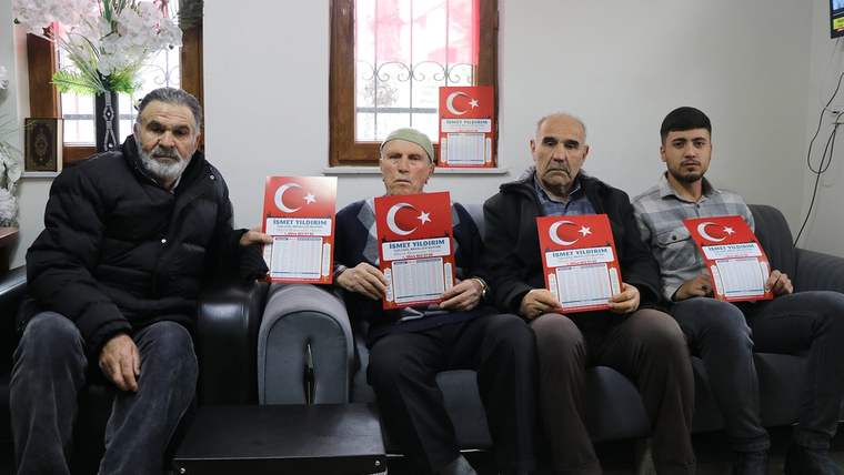 Dört kişi, Türk bayrağı simgeli imsakiye tutarak bir koltukta oturuyor.