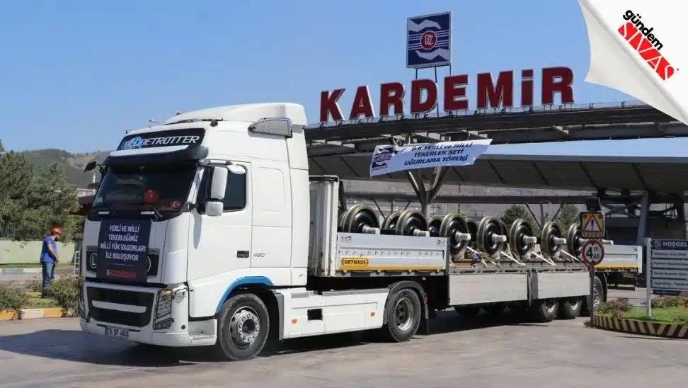 KARDEMİR tabelası önünde, kasasında demir yolu tekerlekleri bulunan beyaz bir kamyon duruyor.
