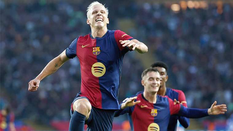 Barcelona forması giyen bir futbolcu sahada kollarını açarken, iki takım arkadaşı arka planda görülüyor.