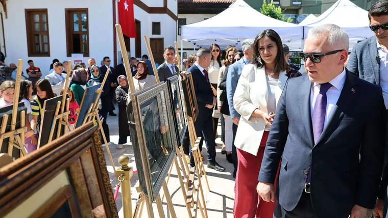 Sergide, çerçevelenmiş resimlerin önünde duran kalabalık bir izleyici grubu yer alıyor.