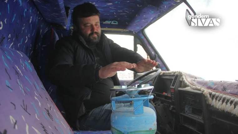 Bir aracın ön koltuğunda oturan kişi, ellerini önündeki mavi piknik tüpünün üzerinde tutuyor.