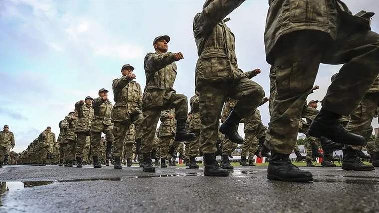 Askeri üniforma giymiş askerler, yürüyüş yaparak eğitim alanında ilerliyor.