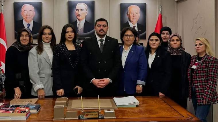 Çalışma masasının arkasında duran sekiz kişi, duvardaki üç portre ve Türk bayraklarıyla birlikte görülüyor.
