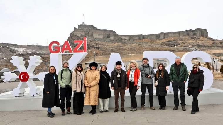 Taş kale önünde, üzerinde “GAZİ” yazılı dekoratif harflerin yanında duran kalabalık grup