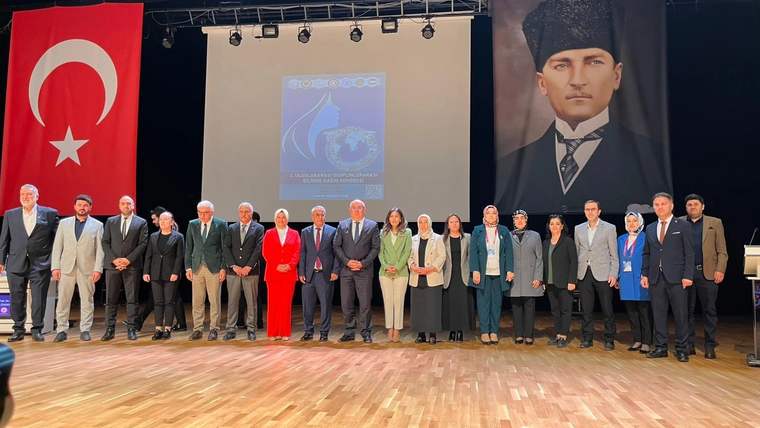 Sahne önünde, katılımcılar ve konuşmacılar bir arada poz veriyor; arka planda Türk bayrağı ve Atatürk portresi var.