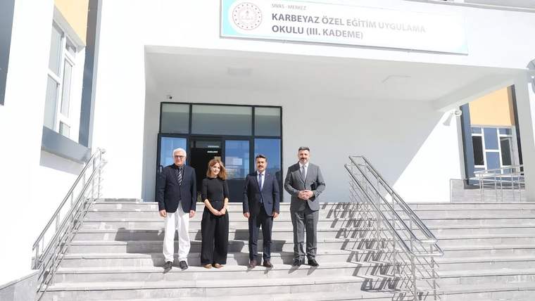 Dört kişi, Karbeyaz Özel Eğitim Uygulama Okulu'nun önünde duruyor. Okul binası modern bir mimariye sahip.