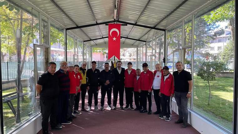 Camlarla çevrili spor alanında, Türk bayrağının altında yan yana duran kalabalık bir grup görülüyor.