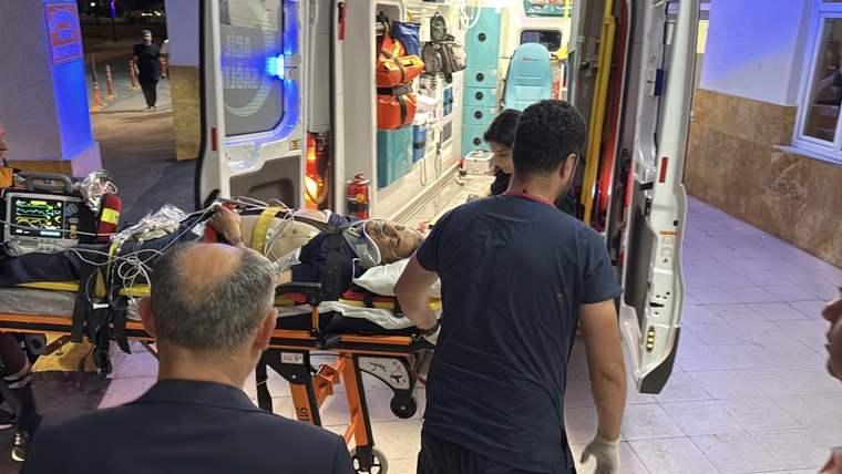 Ambulansın arka kapısında sedye üzerinde bir hasta taşınıyor, yanında sağlık çalışanları var.