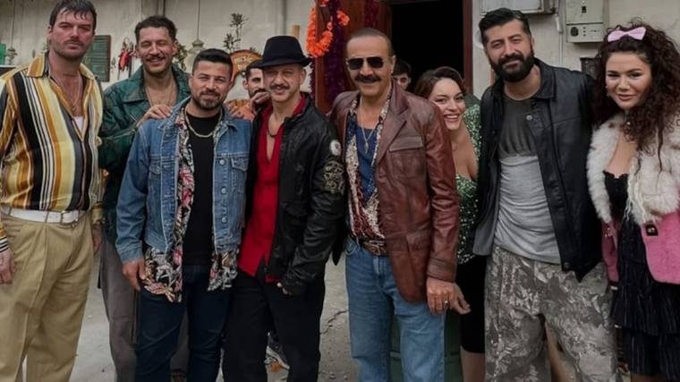 Bir binanın girişinde, farklı kıyafetler giyen dokuz kişi yan yana durarak kameraya poz veriyor.