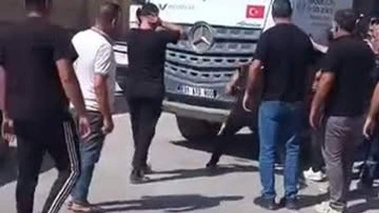 Bir grup insan, bir beton mikserinin etrafında toplanmış, bazıları mikseri yumrukluyor.