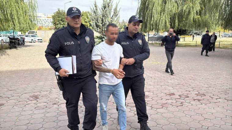 Yüzü bulanıklaştırılmış bir erkek, iki polis memurunun arasında kaldırımda yürürken görüntüleniyor.
