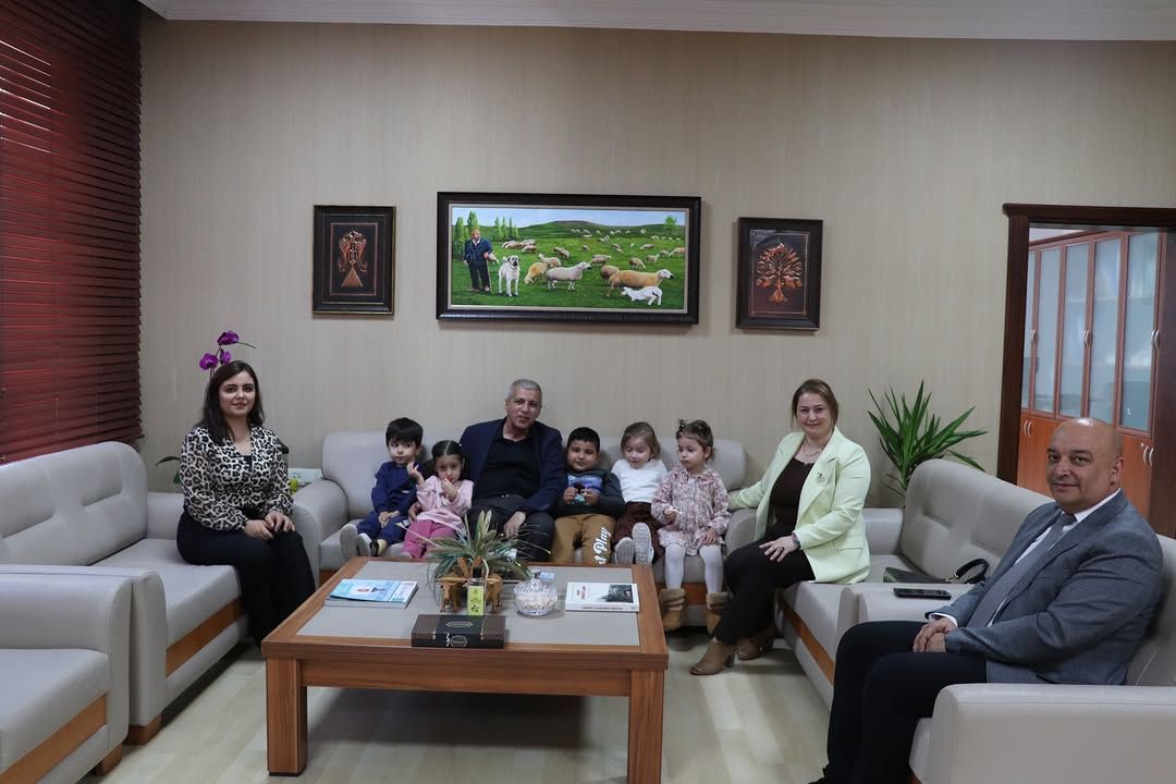 Bir ofiste koltuklarda oturan yetişkinler ve çocuklar, sehpanın önünde birlikte poz veriyor.
