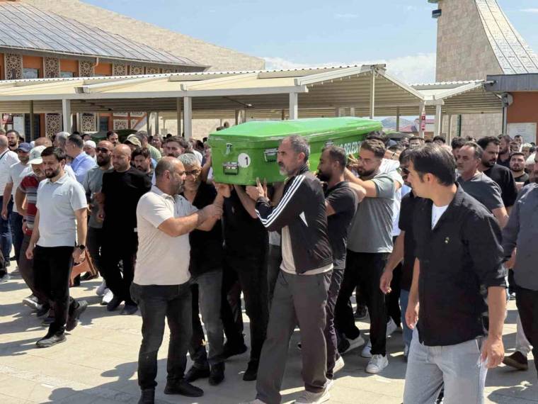 Kalabalık bir grup erkek, açık havada yeşil bir tabutu taşıyarak avluda ilerliyor.