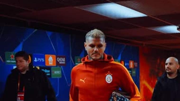 Galatasaray armalı kırmızı eşofmanlı bir kişi, koridorda elinde desenli bir çantayla yürürken görülüyor.