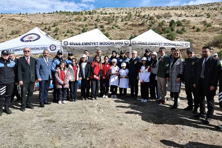Kurak arazide, üzerinde Sivas Emniyet Müdürlüğü yazan çadırların önünde yetişkinler ve çocuklar toplu duruyor.