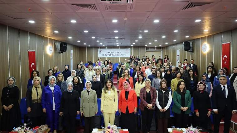 Koruyucu aile farkındalık toplantısında bir araya gelen kalabalık grup, sahnede poz veriyor.